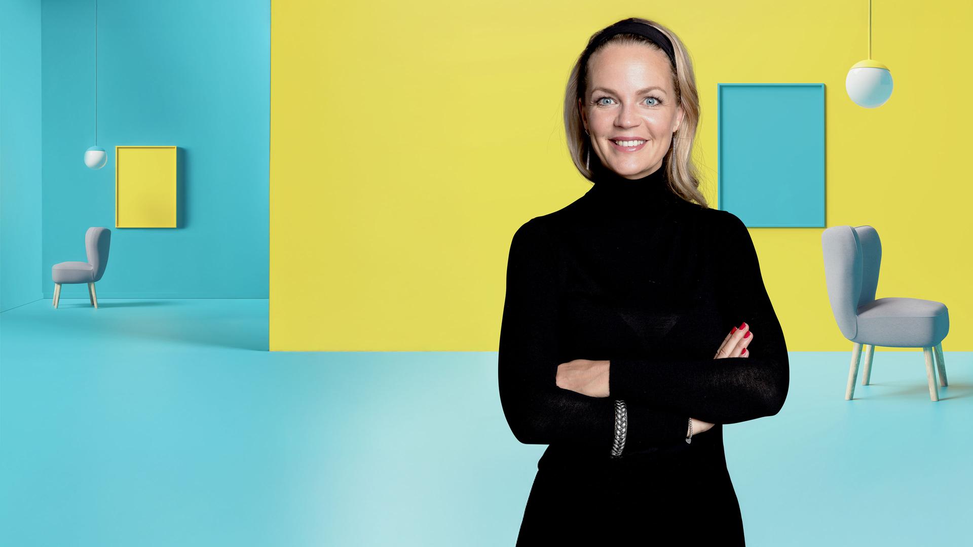 Eva Brenner vor gelb-blauem Hintergrund, rechts von ihr die Animation eines Wohnbereichs mit Stühlen, Bildern und Lampen.