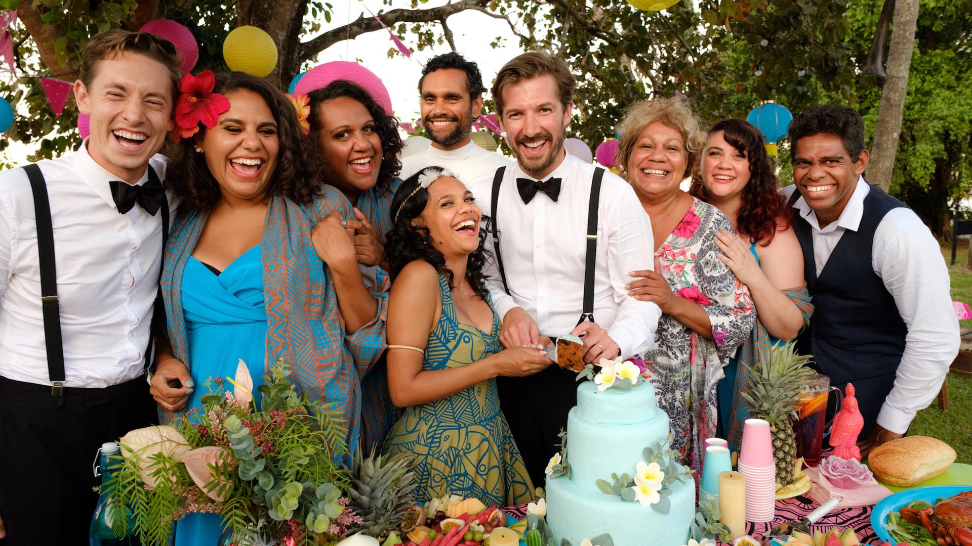 Mit dem Brautpaar Lauren (Miranda Tapsell, 3.v.l.) und Ned (Gwilym Lee, M.) freuen sich die Hochzeitsgäste: Neds Bruder Robbie (Matt Crook, l.), die Brautjungfern Dana (Elaine Crombie, l.), Kailah (Dalara Williams; 2.v.l.) und Ronelle (Shari Sebbens, r.), der Pfarrer (Rob Collins, Mitte hinten), Cousin Braydon (Shaka Cook, r.) und Tante Bree (Tessa Rose, 2.v.r.).