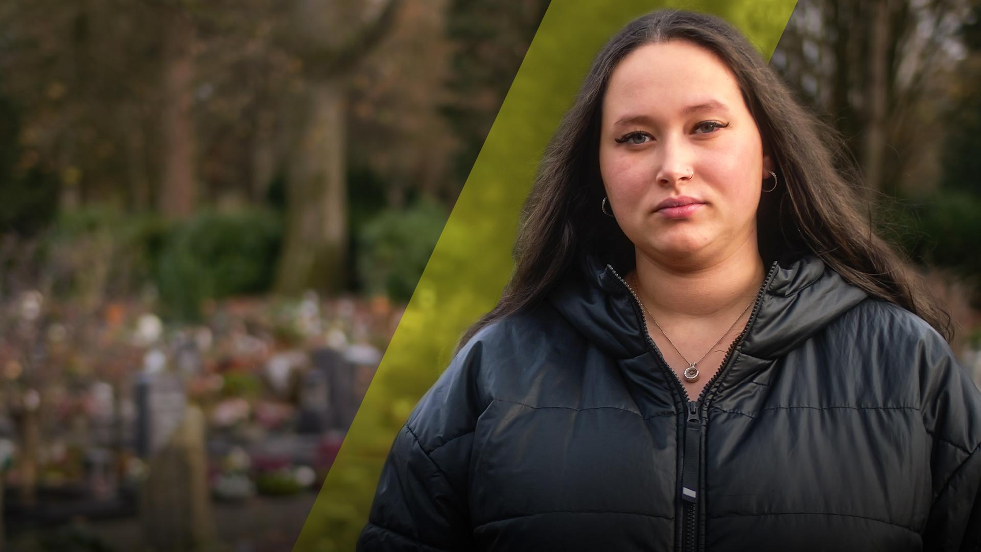 Eine junge Frau schaut traurig nach vorne. Im Hintergrund ist ein Friedhof zu sehen. 