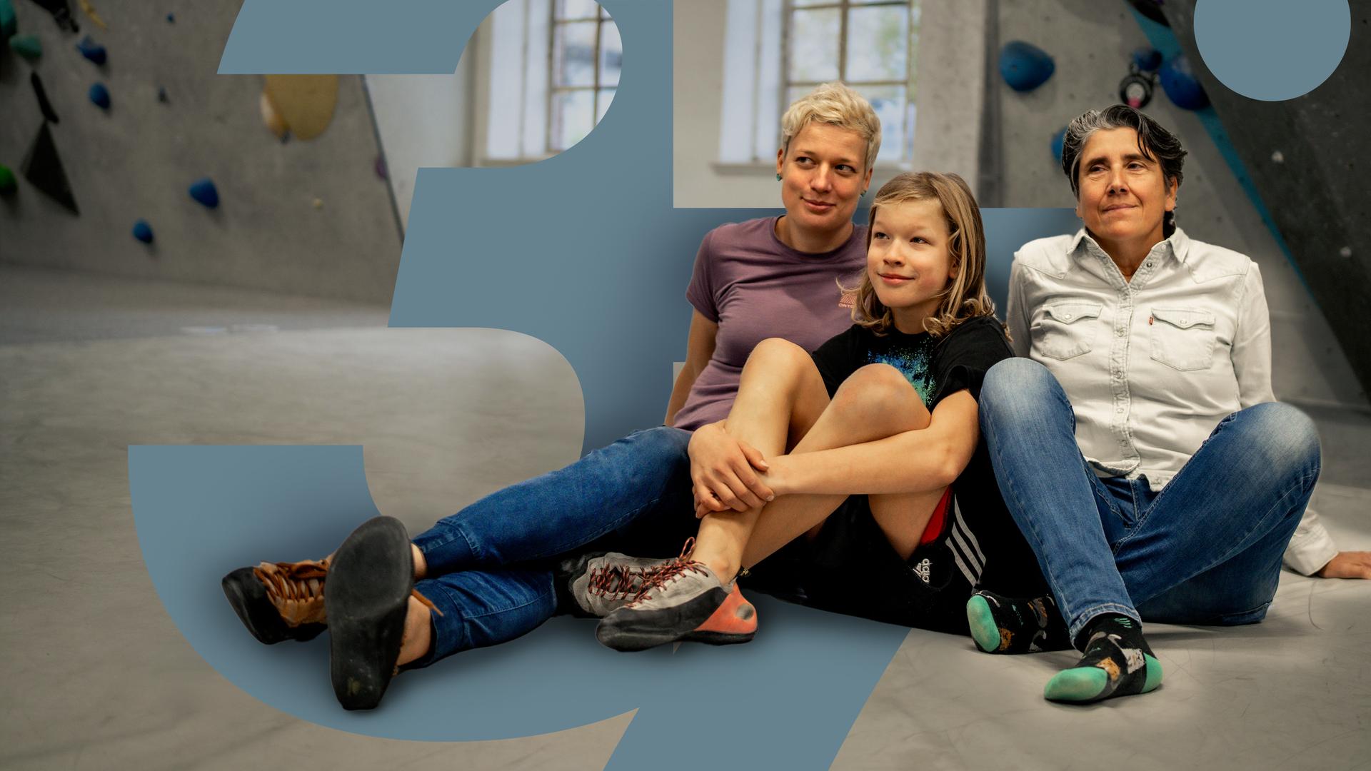 In der Boulderhalle sitzen Judith und Andrea zusammen auf dem Boden. Ihr gemeinsamer Sohn Oskar sitzt in der Mitte.