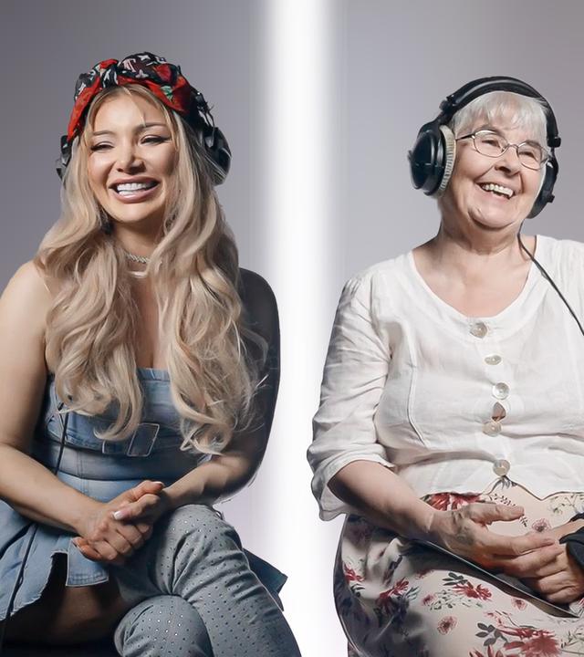 Eine junge und eine alte Frau sitzen nebeneinander und lachen. Sie tragen Kopfhörer.