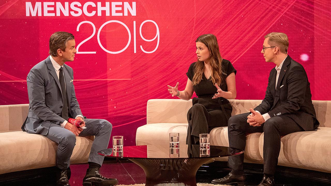 "Menschen 2019": Markus Lanz im Gespräch mit Luisa Neubauer und Philipp Amthor. Luisa Neubauer spricht gestikulierend, während die beiden Männer sie ansehen.