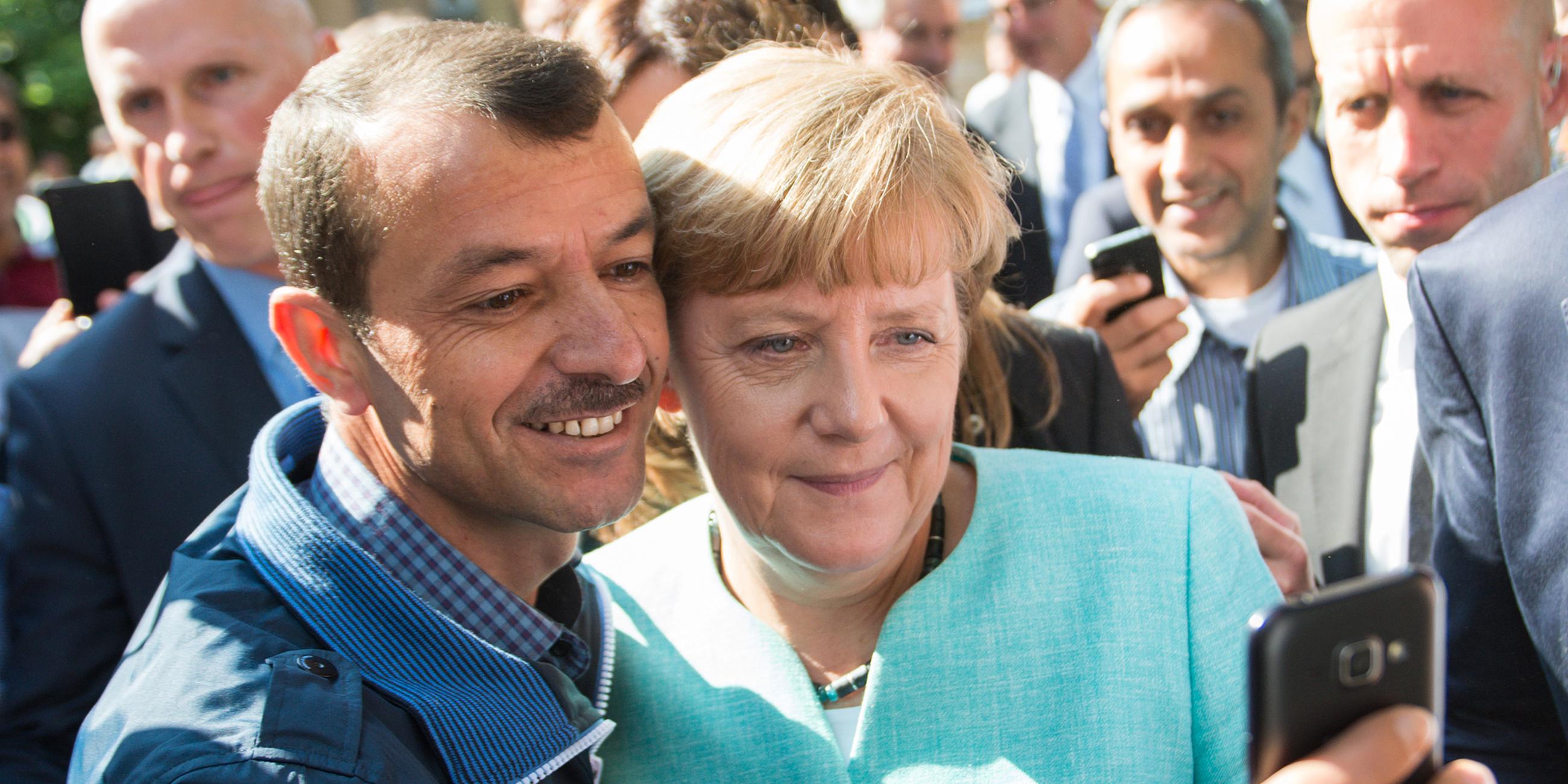 Bundeskanzlerin Angela Merkel lässt sich 2015, nach dem Besuch einer Erstaufnahmeeinrichtung für Asylbewerber, für ein Selfie zusammen mit einem Flüchtling fotografieren.