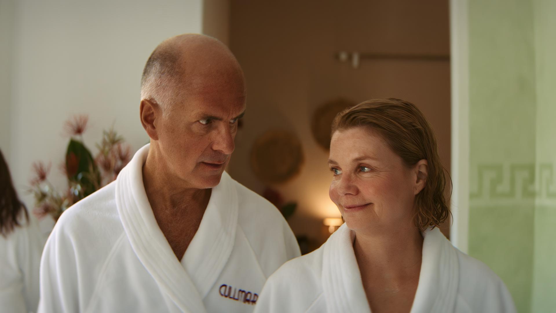 "Merz gegen Merz: Geständnisse": Anne (Annette Frier) und Erik (Christoph Maria Herbst) laufen lächelnd in Bademänteln durch den Spa-Bereich des Hotels "Cullmar".