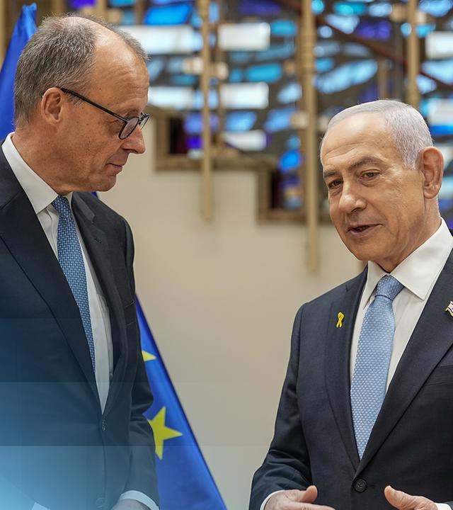 Friedrich Merz und Benjamin Netanjahu sprechen vor der deutschen, israelischen und europäischen Flagge miteinander.