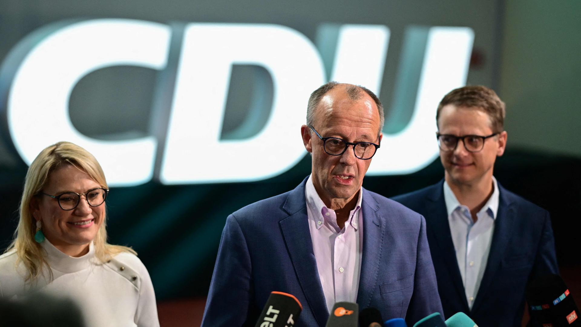 Friedrich Merz in der Mitte an einem Mikrofon. Carsten Linnemann und Christina Stumpp stehen neben ihm.