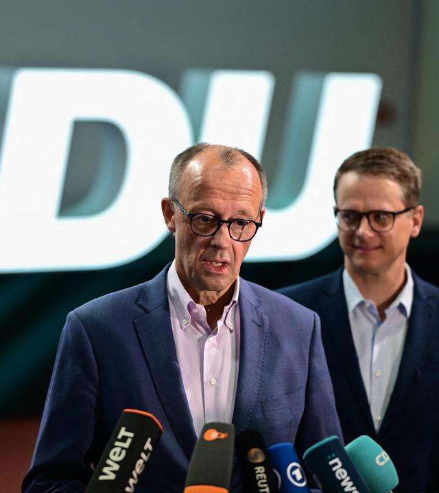 Friedrich Merz in der Mitte an einem Mikrofon. Carsten Linnemann und Christina Stumpp stehen neben ihm.