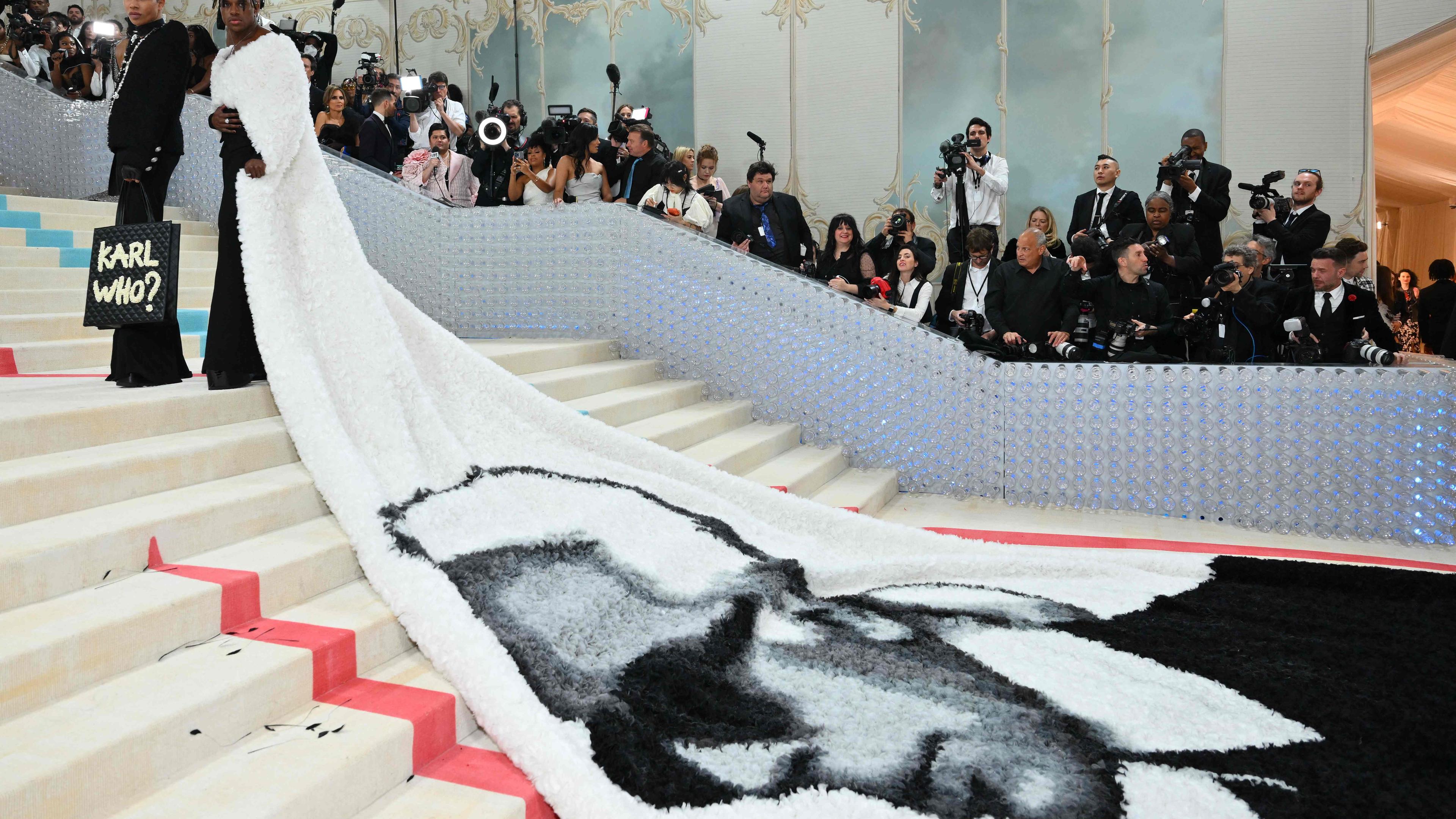Eine Frau läuft auf der Met Gala eine Treppe hoch - auf ihre Kleidschleppe ist ein Bild von Karl Lagerfeld gedruckt. 