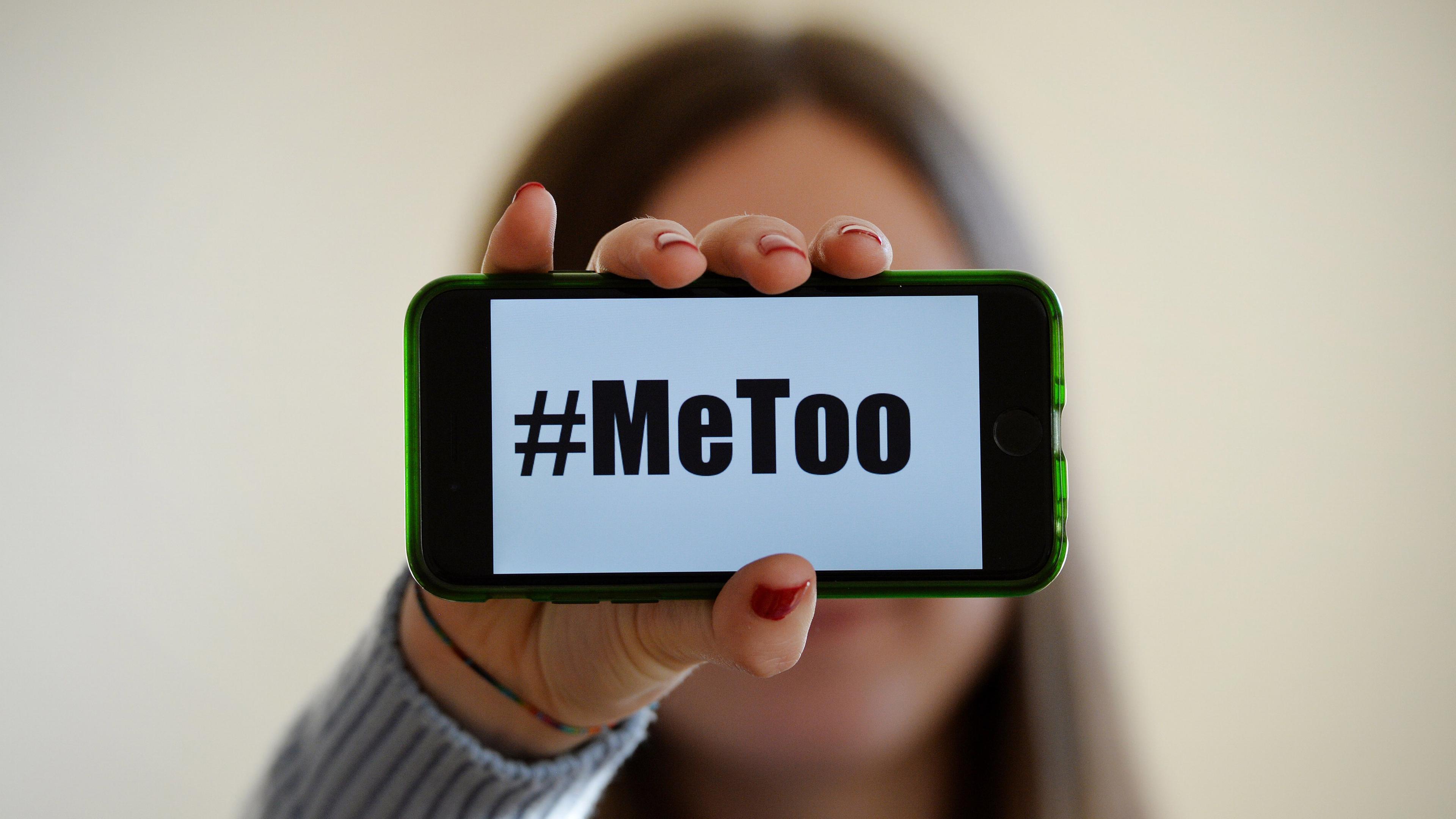 Frauenhand hält Handy, auf dem Bildschirm steht groß #MeToo