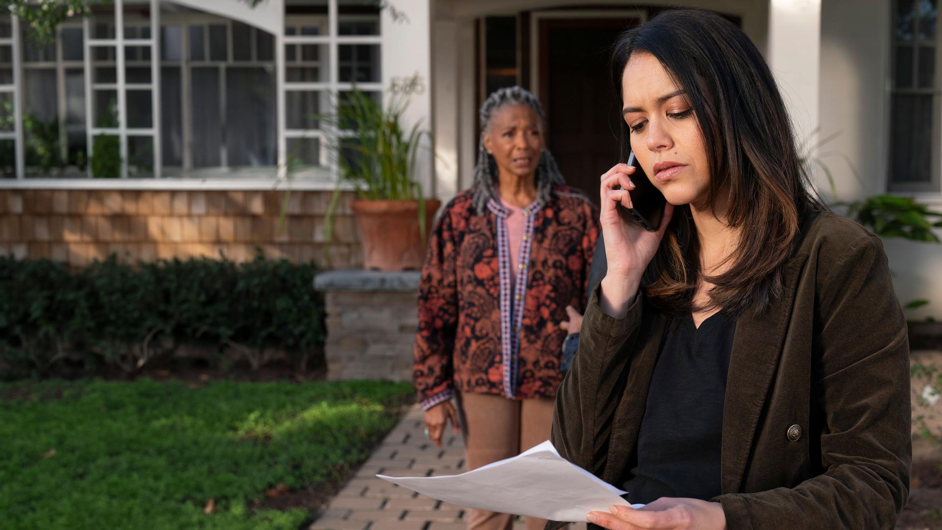 "The Rookie - Meuterei und Kopfgeld": Officer Angela Lopez (Alyssa Diaz) steht gemeinsam mit Ruth Harper (Margaret Avery) vor einem Haus. Lopez hält ein Blatt Papier in der einen, ein Smartphone in der anderen Hand. Ihr Blick ist kritisch auf das Dokument gerichtet. Ruth Harper schaut erwartungsvoll zu Lopez.