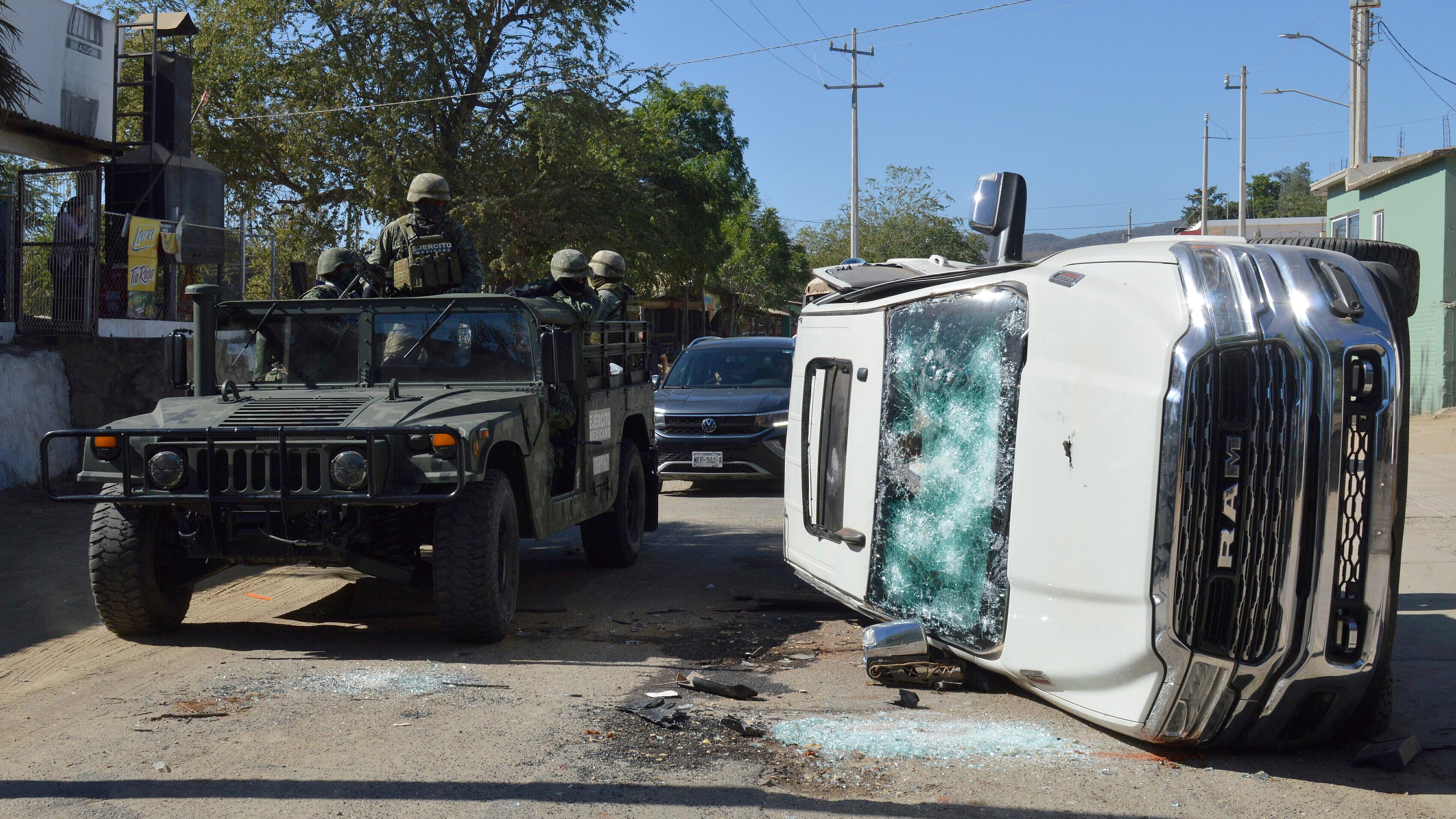 Soldaten der Armee fahren am Samstag, den 07.01.2023, an einem zerstörten Fahrzeug in den Straßen von Jesus Maria (Mexiko) vorbei