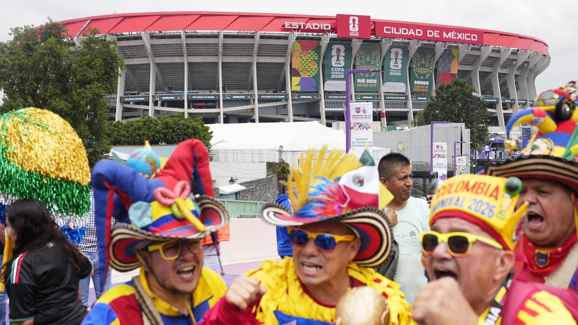 Vor dem Fußballstadion in Mexiko City stehen wie zum Karneval bunt gekleidete Männer mit Sonnebrillen und großen aufgeputzen Hüten.