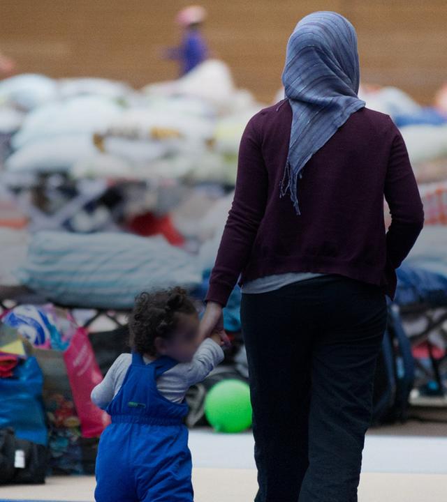 Eine Frau läuft mit einem Kind an der Hand durch eine Flüchtlingsunterkunft