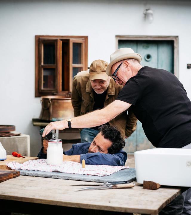 Drei Männer beobachten sehr interressiert ein Glas mit weissem Inhalt