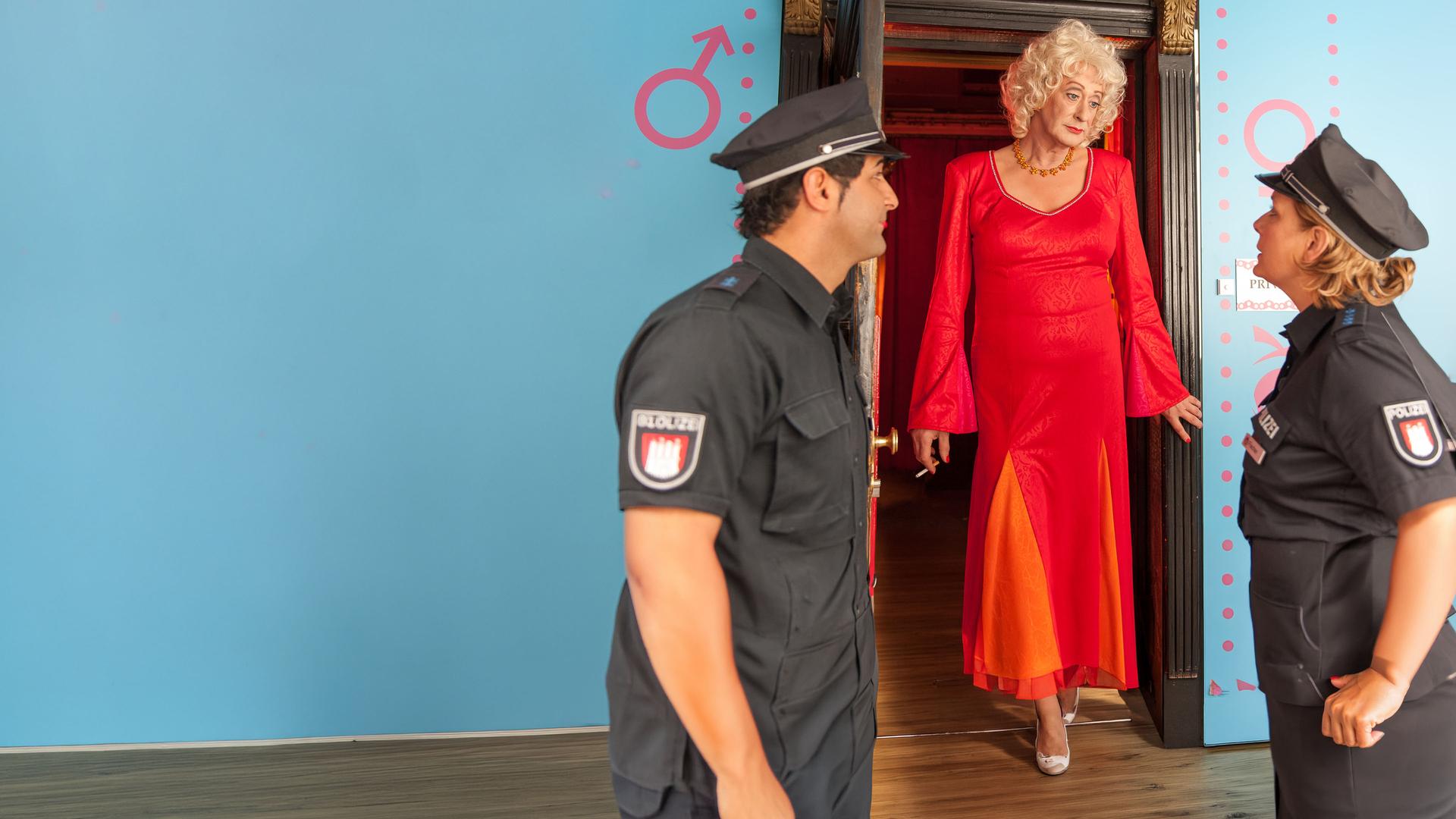 "Notruf Hafenkante: Minderheitenkrieg": Clara Corn (Lilo Wanders) steht zwischen den Polizisten Claudia (Janette Rauch) und Tarik (Serhat Cokgezen) in einer geöffneten Wohnungstür.