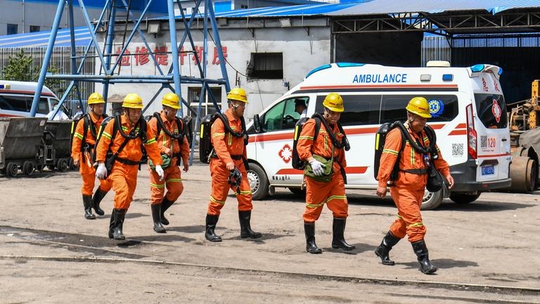 Rettungskräfte in orangenen Anzügen laufen vor einem Krankenwagen.