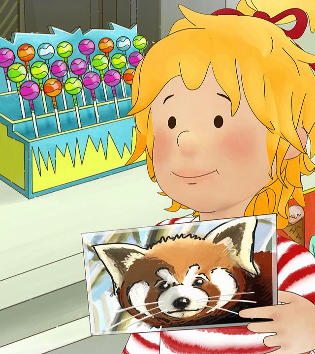 Conni steht im Zoo an der Kasse. Sie hält eine Postkarte mit einem roten Panda in der Hand.