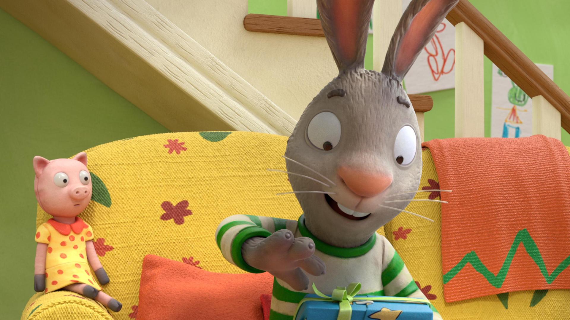 Pip sitzt auf einem Sofa und beginnt freudig, ein in Sternenpapier eingewickeltes Geschenk auszupacken.