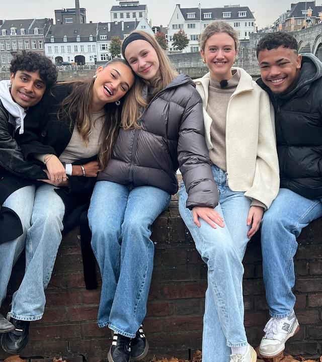 Malik, Sofia, Toni, Emma und Chinedu sitzen auf einer Mauer - im Hintergrund die Stadt