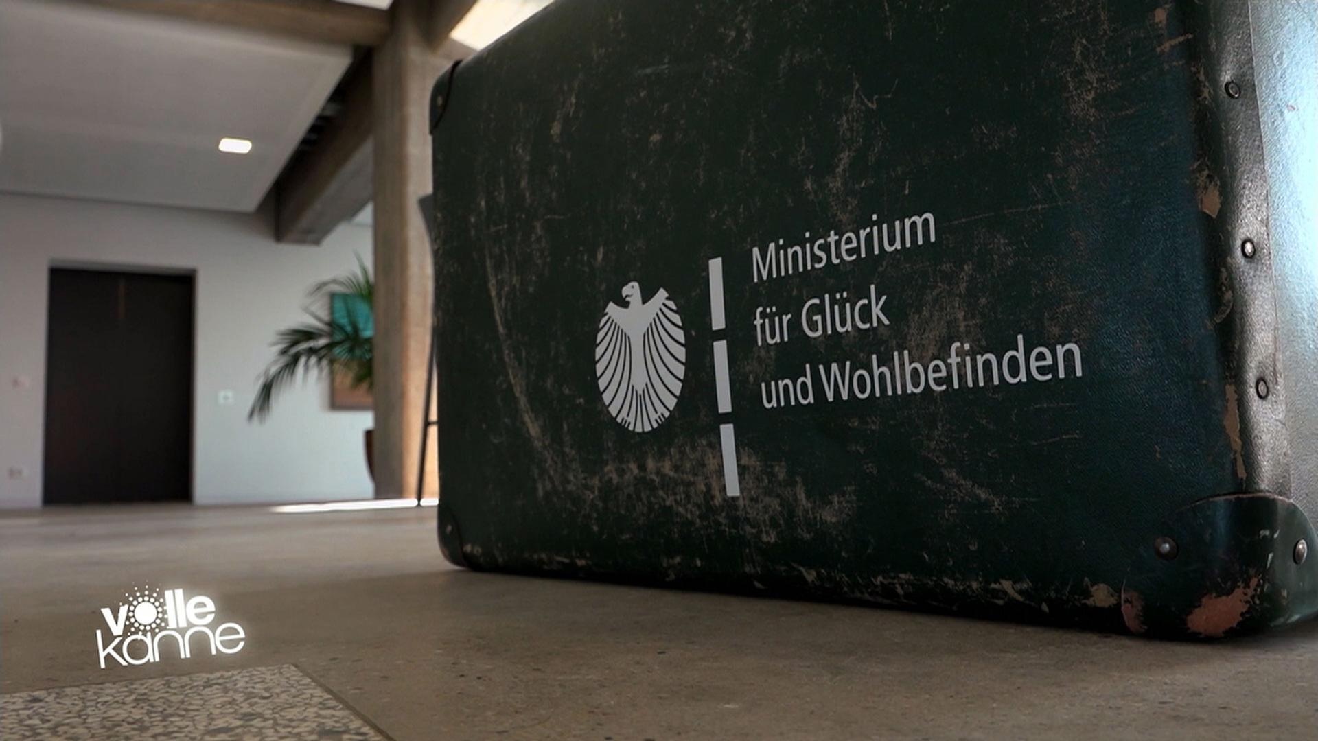 Koffer mit der Aufschrift "Ministerium für Glück und Wohlbefinden"