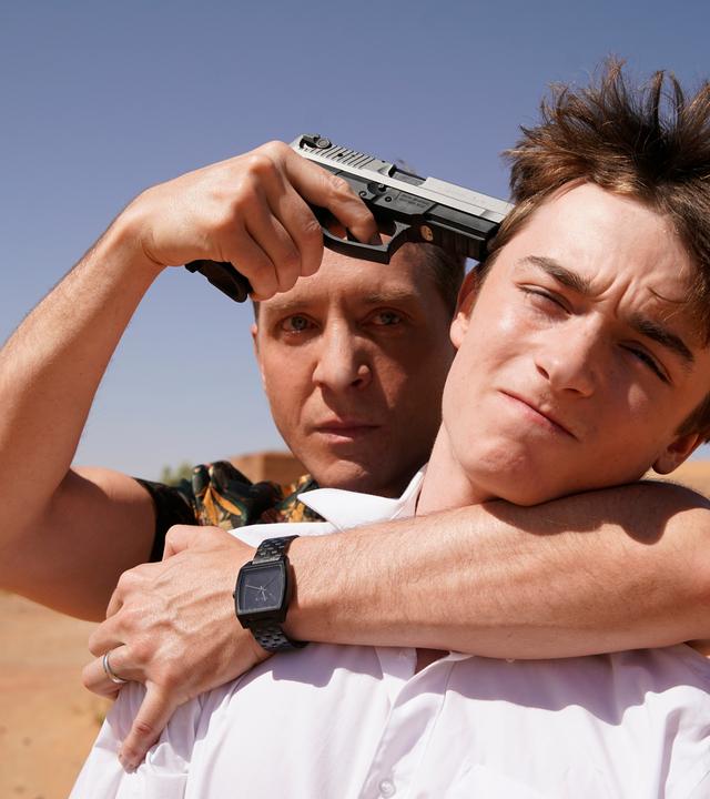 "Mirage - Gefährliche Lügen": Doug (Shawn Doyle) steht hinter Zack (Thomas Chomel). Er hat einen Arm um den Hals des Jungen gelegt und hält ihm eine Waffe an den Kopf.