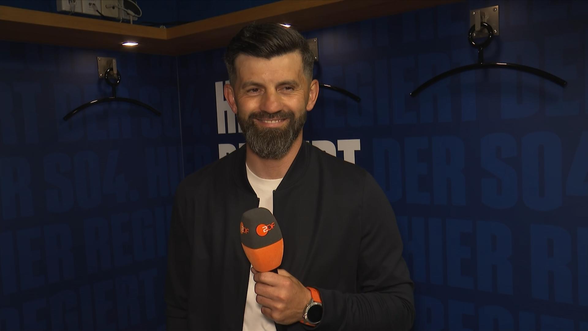 Der Cheftrainer des FC Schalke 04, Miron Muslić, steht beim ZDF-Interview lächelnd in der Kabine der Knappen