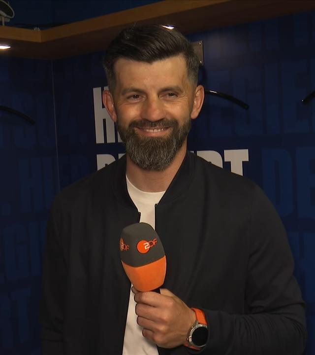 Der Cheftrainer des FC Schalke 04, Miron Muslić, steht beim ZDF-Interview lächelnd in der Kabine der Knappen