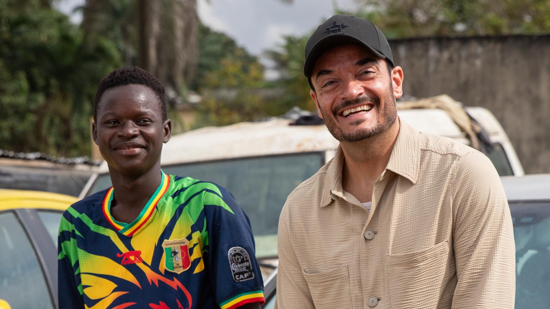 "Die große Weihnachtsshow": Gemeinsam mit Pierre Dougnon, der eine Ausbildung als KFZ-Mechaniker in Abidjan (Elfenbeinküste) macht, sitzt Giovanni Zarrella auf der Motorhaube eines silbergrauen PKW. Beide schauen lächelnd in die Kamera.
