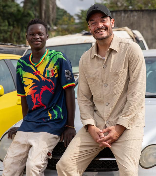 "Die große Weihnachtsshow": Gemeinsam mit Pierre Dougnon, der eine Ausbildung als KFZ-Mechaniker in Abidjan (Elfenbeinküste) macht, sitzt Giovanni Zarrella auf der Motorhaube eines silbergrauen PKW. Beide schauen lächelnd in die Kamera.