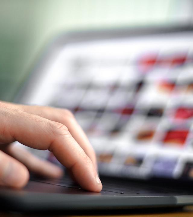 Die Finger einer Hand auf dem Tastatur eines geöffneten Laptops.