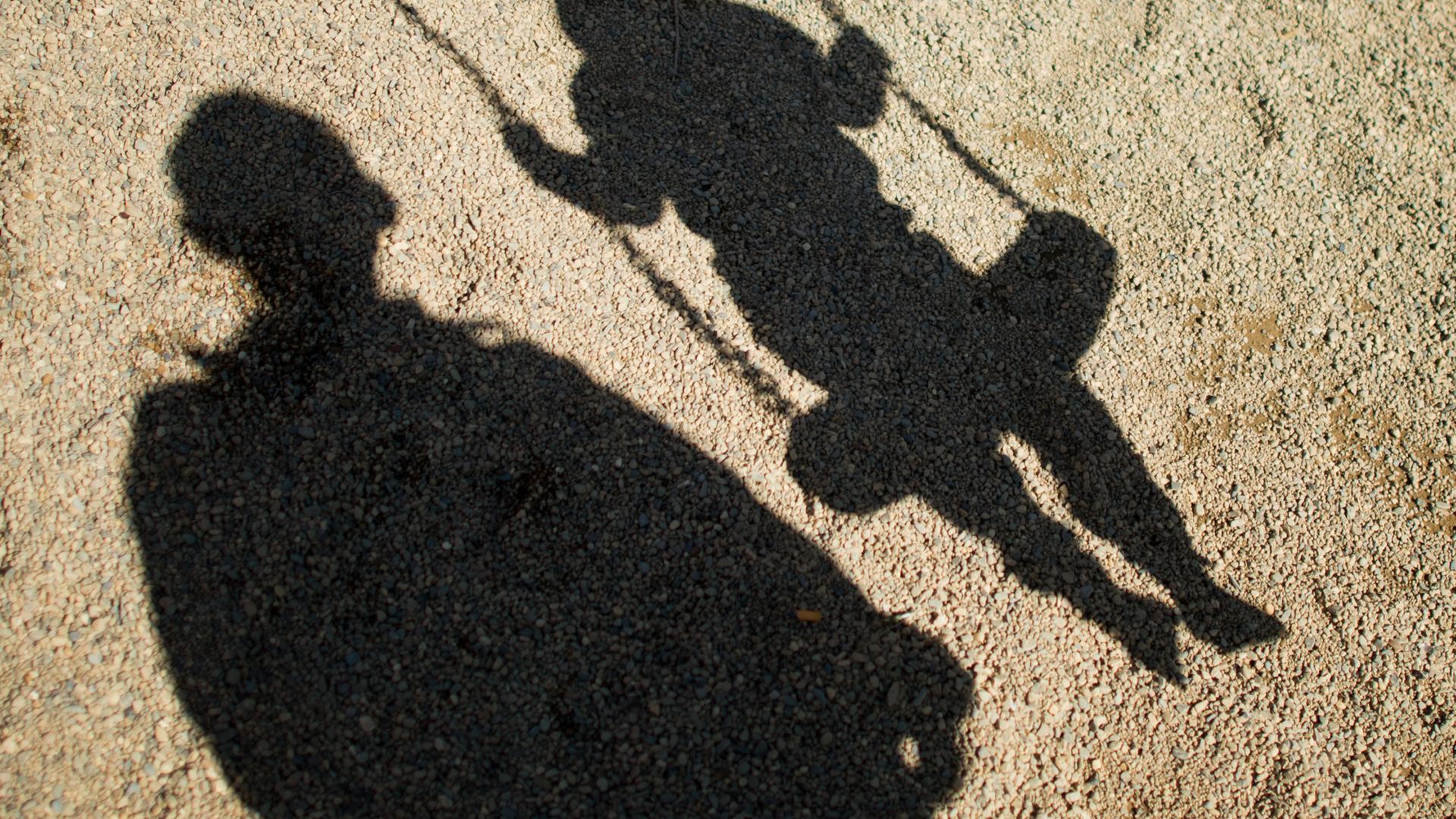 Die Schatten eines Mannes und eines Kindes auf einer Schaukel.