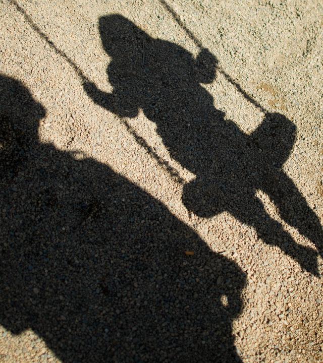 Die Schatten eines Mannes und eines Kindes auf einer Schaukel.