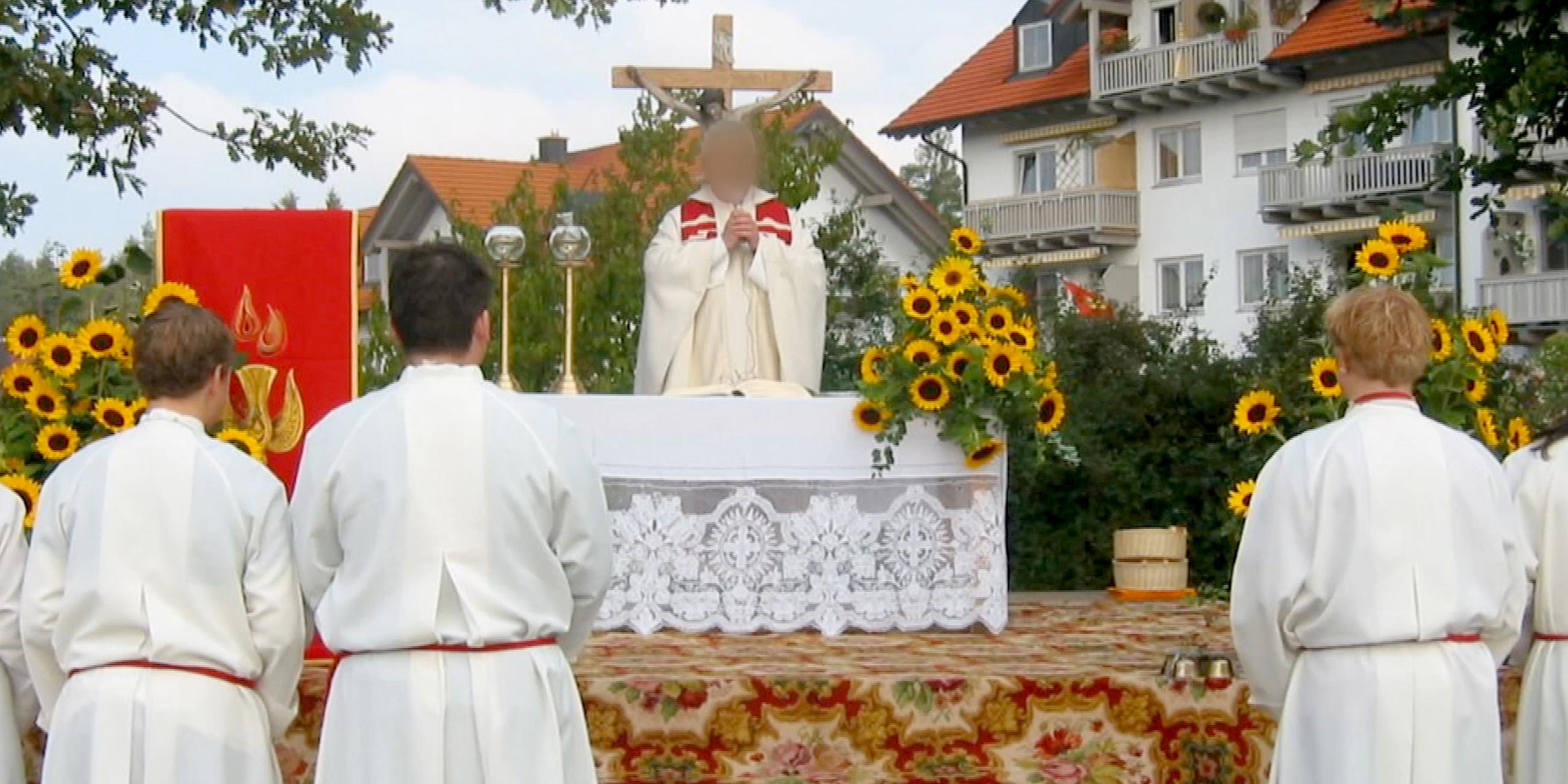 Screenshot aus Video: Eine Andacht im Freien, ein Pfarrer in der Bildmitte (Gesicht verpixelt), Messdiener im Vordergrund