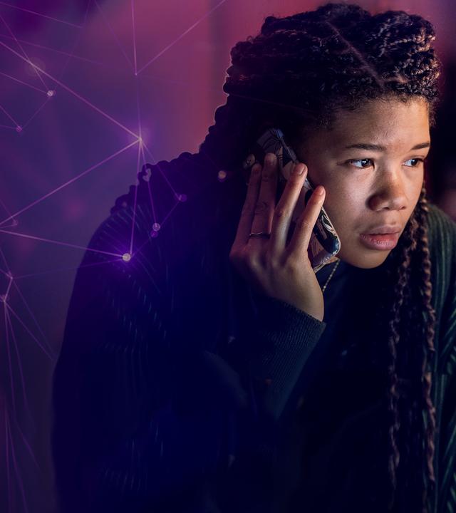 Nahaufnahme: June (Storm Reid) blickt angespannt mit ihrem Smartphone am Ohr auf einen nicht im Bild befindlichen Computerbildschirm, der ihr Gesicht erleuchtet.