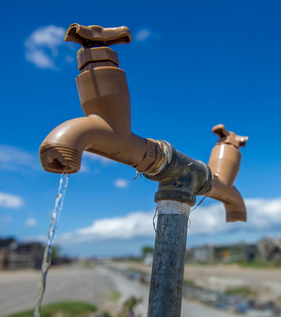Symbolbild für Wasserknappheit: Wasserhahn im Feld. Trinkwasser fließt. 