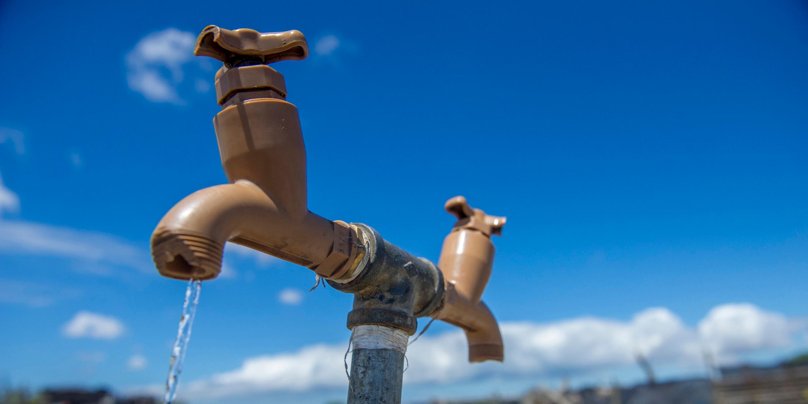 Symbolbild für Wasserknappheit: Wasserhahn im Feld. Trinkwasser fließt. 