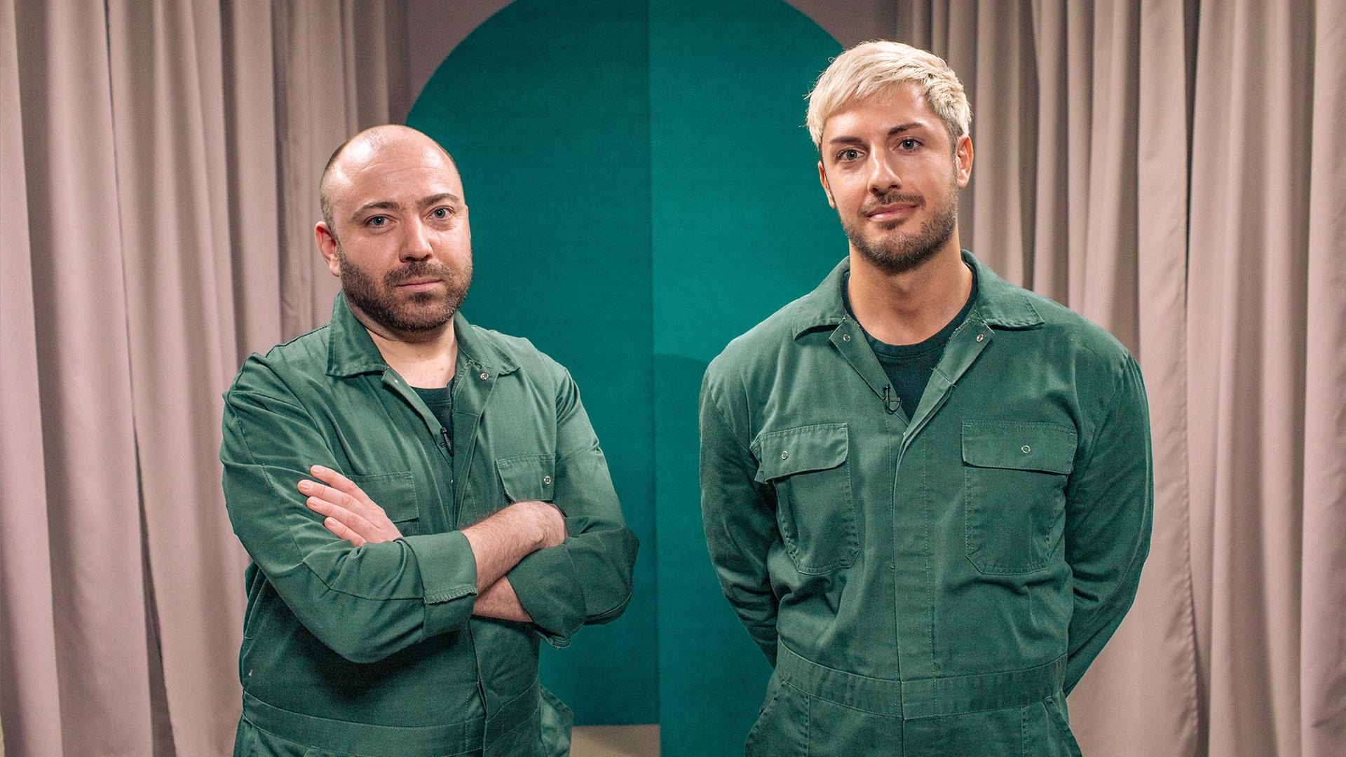 Zwei Männer in grünen Overalls blicken in die Kamera.