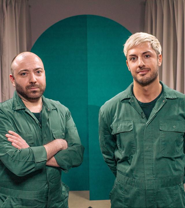 Zwei Männer in grünen Overalls blicken in die Kamera.