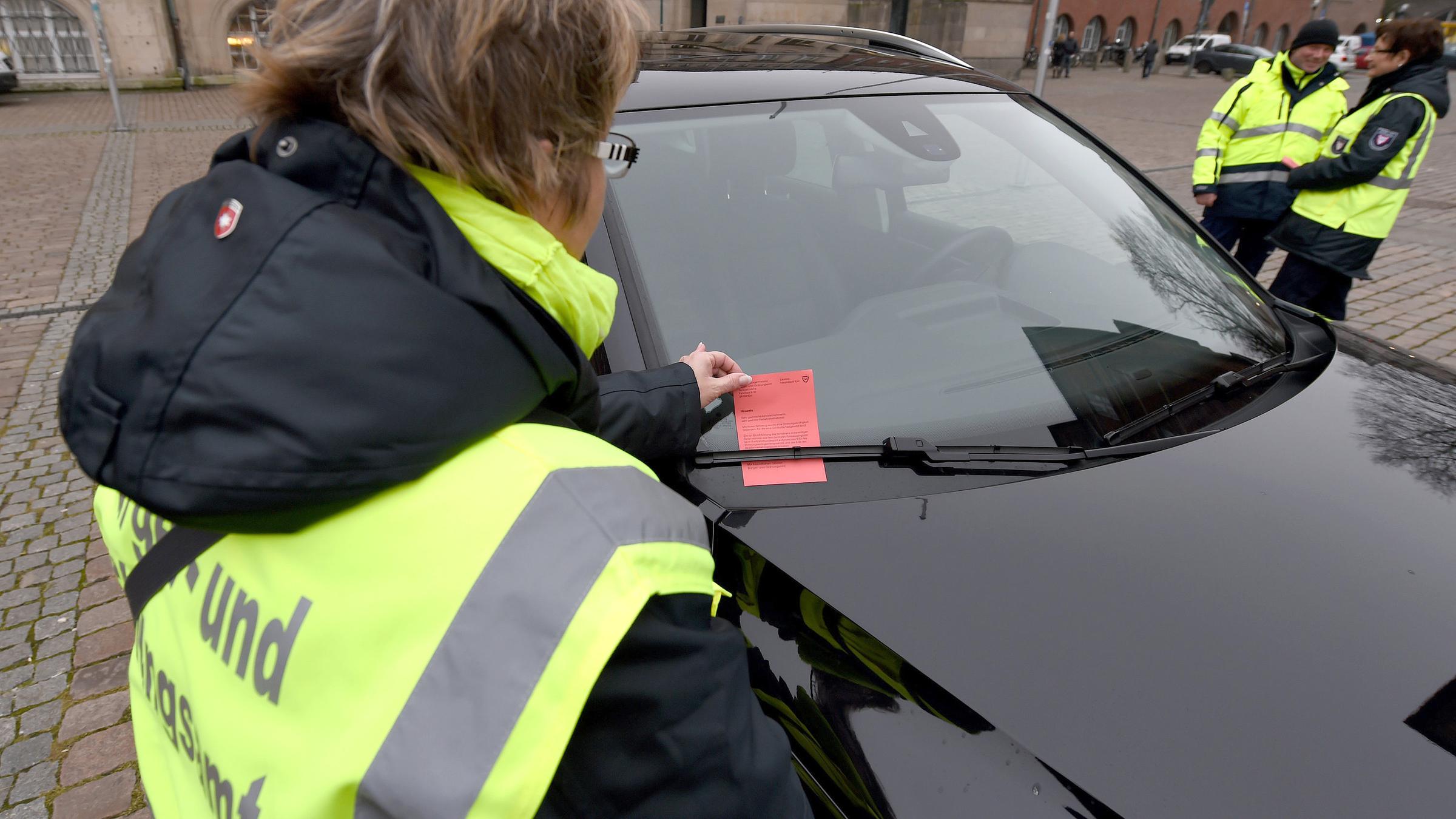 Mitarbeiterin des Ordnungsamtes befestigt einen Verwarnzettel für Falschparker