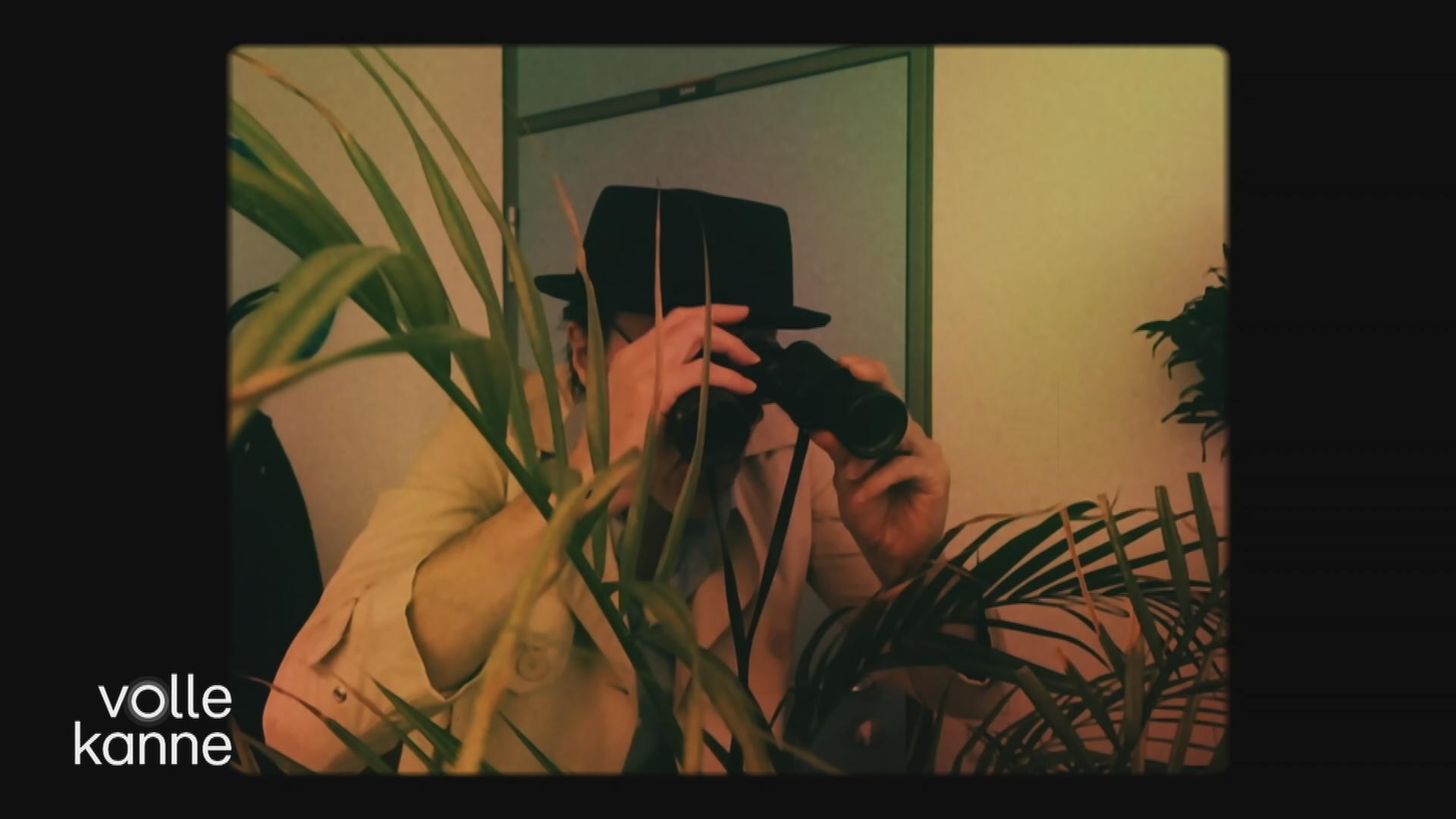 Mann mit Hut un Fernglas spioniert durch Pflanze