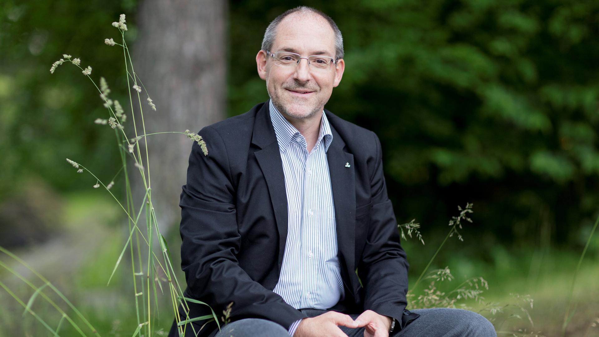 Prof. Christian Rutishauser sitzt im grünen im Hintergrund ist unscharf ein Baum zu sehen. 
