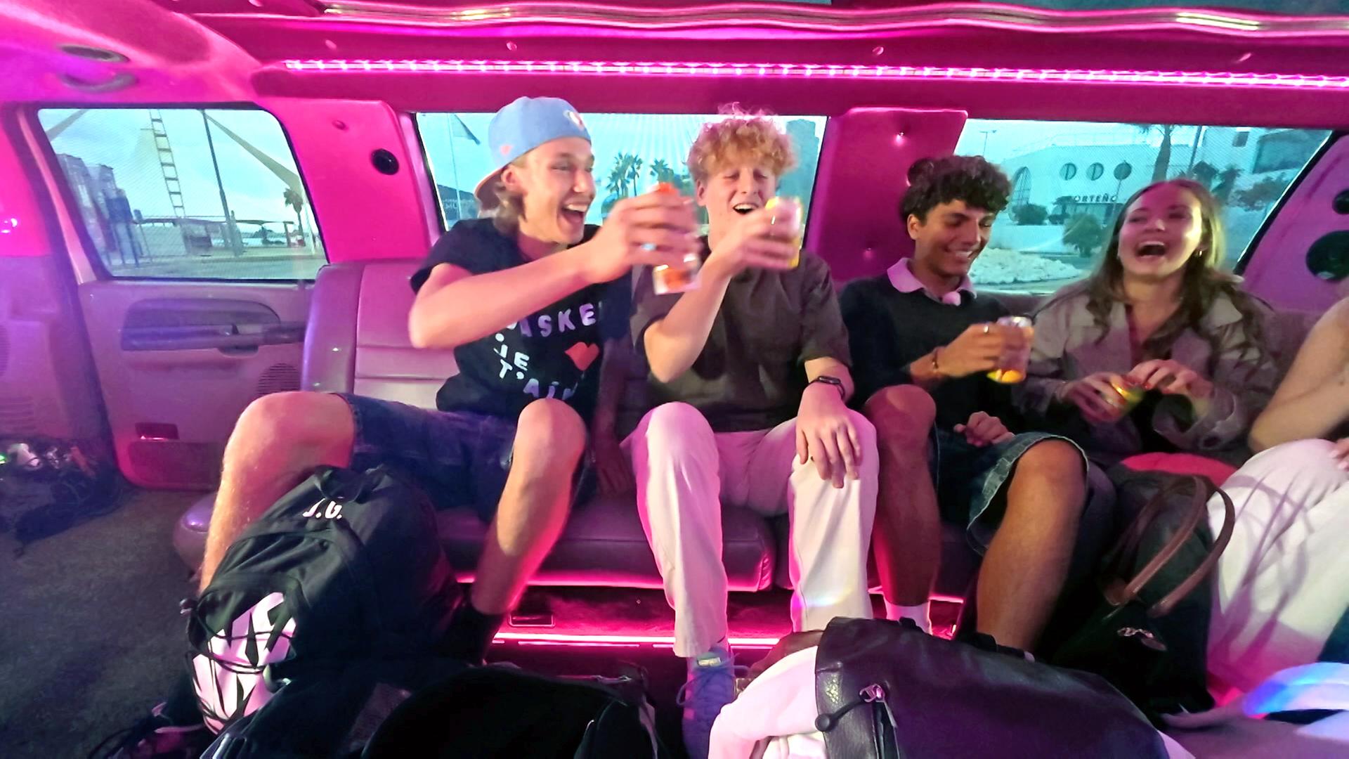 v.l.n.r. Jan, Rufus, Adrian und Lina-Marie sitzen in einer rosa ausgelichteten Limousine, lachen und stoßen mit Getränken an.