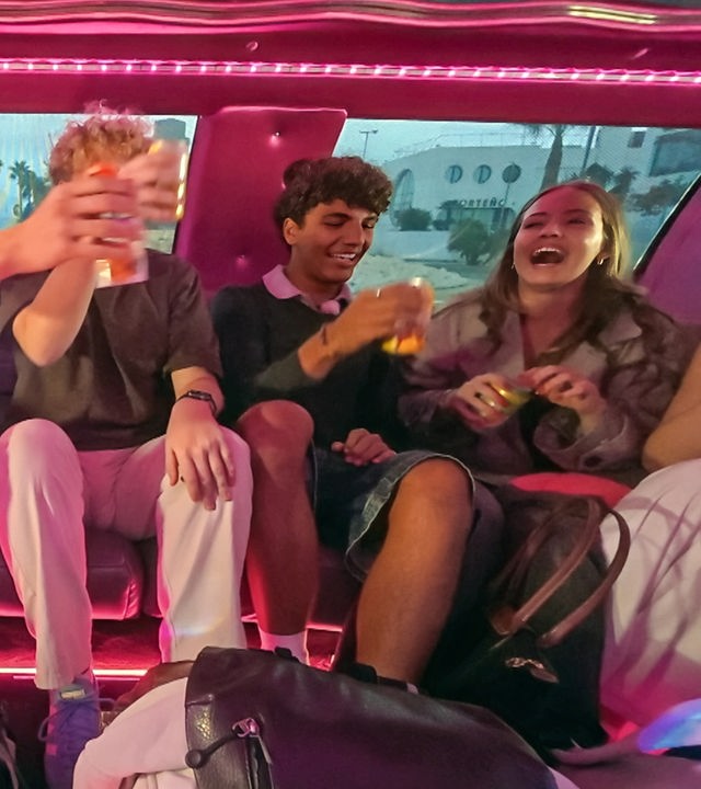 v.l.n.r. Jan, Rufus, Adrian und Lina-Marie sitzen in einer rosa ausgelichteten Limousine, lachen und stoßen mit Getränken an.