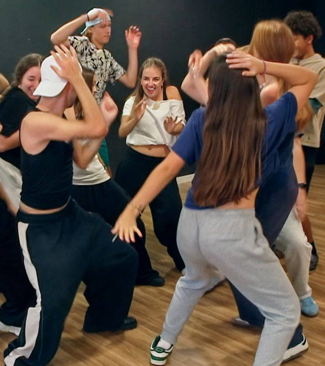 Eine Gruppe gemischtgeschlechtlicher Jugendlicher stehen auf einem Haufen in einem Tanzraum und tanzen ausgelassen.