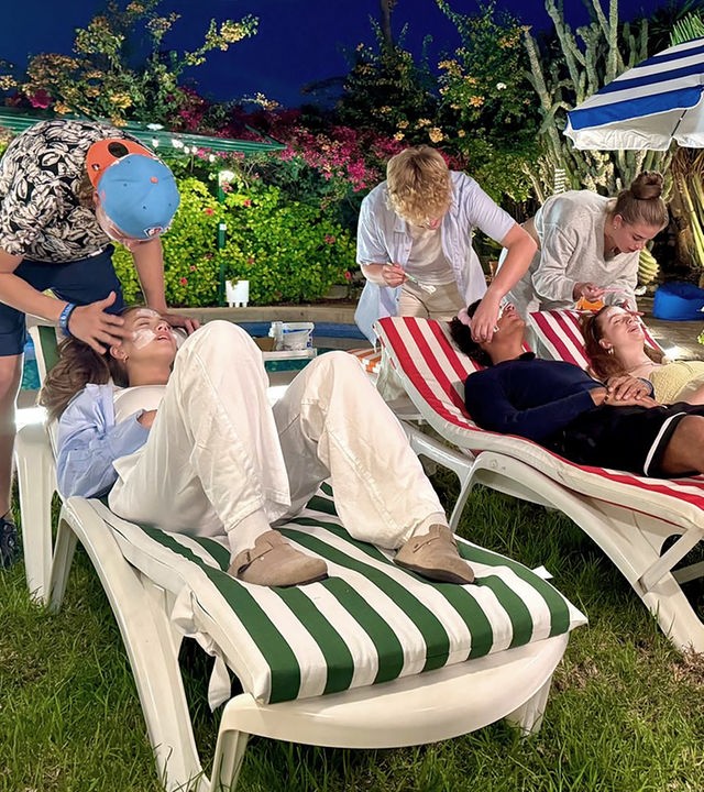 Auf Liegestühlen liegen v.l.n.r. Lina-Marie, Adrian und Marie, welche von v.l.n.r. Jan, Rufus und Lenja gepflegt werden, die jeweils hinter den Stühlen stehen. Sie tragen ihnen Gesichtsmasken auf. Im Hintergrund ist ein Pool zu sehen.