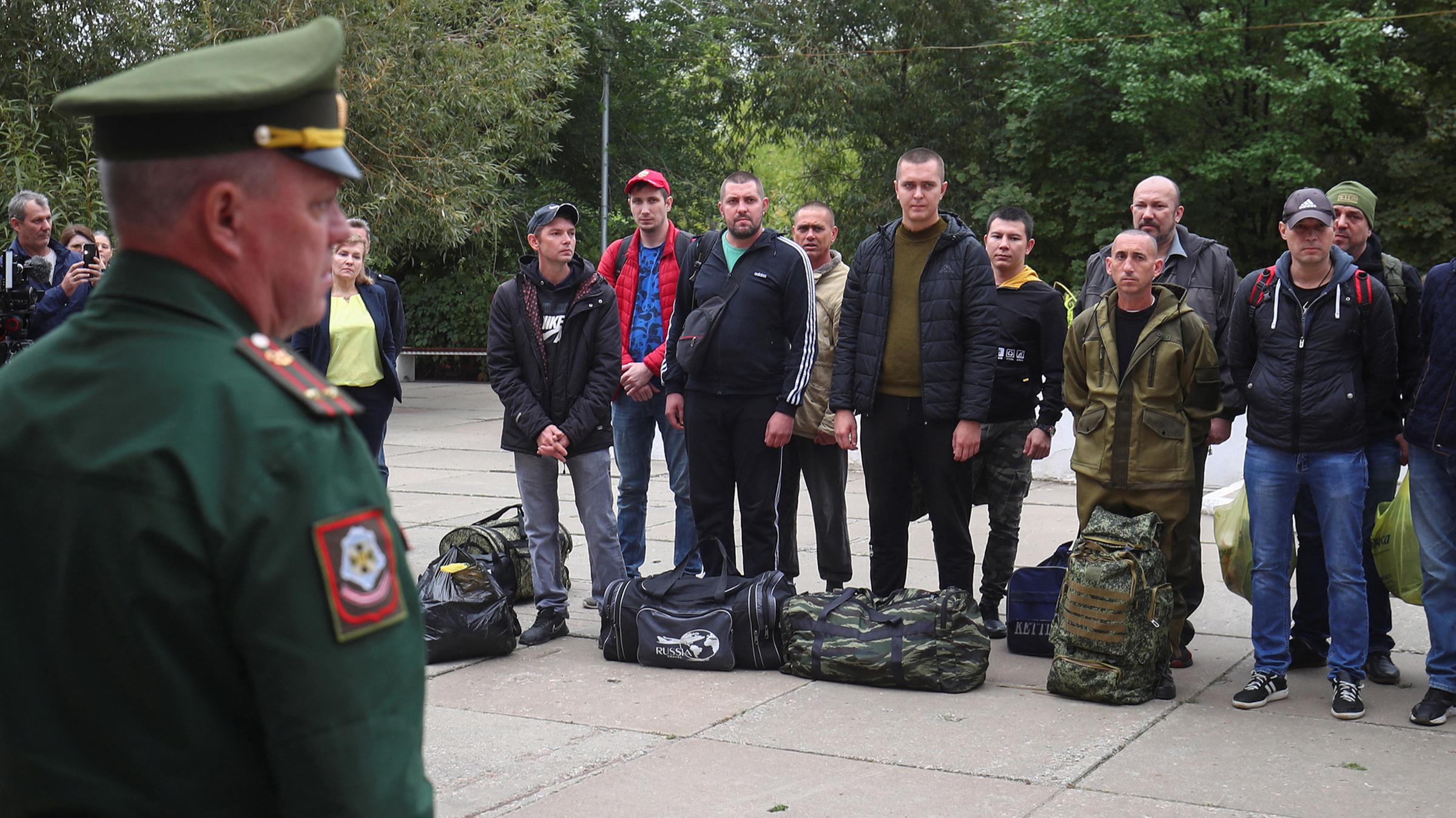 Eine Gruppe von russischen Reservisten steht bei ihrer Einberufung vor einem Mann in Uniform.