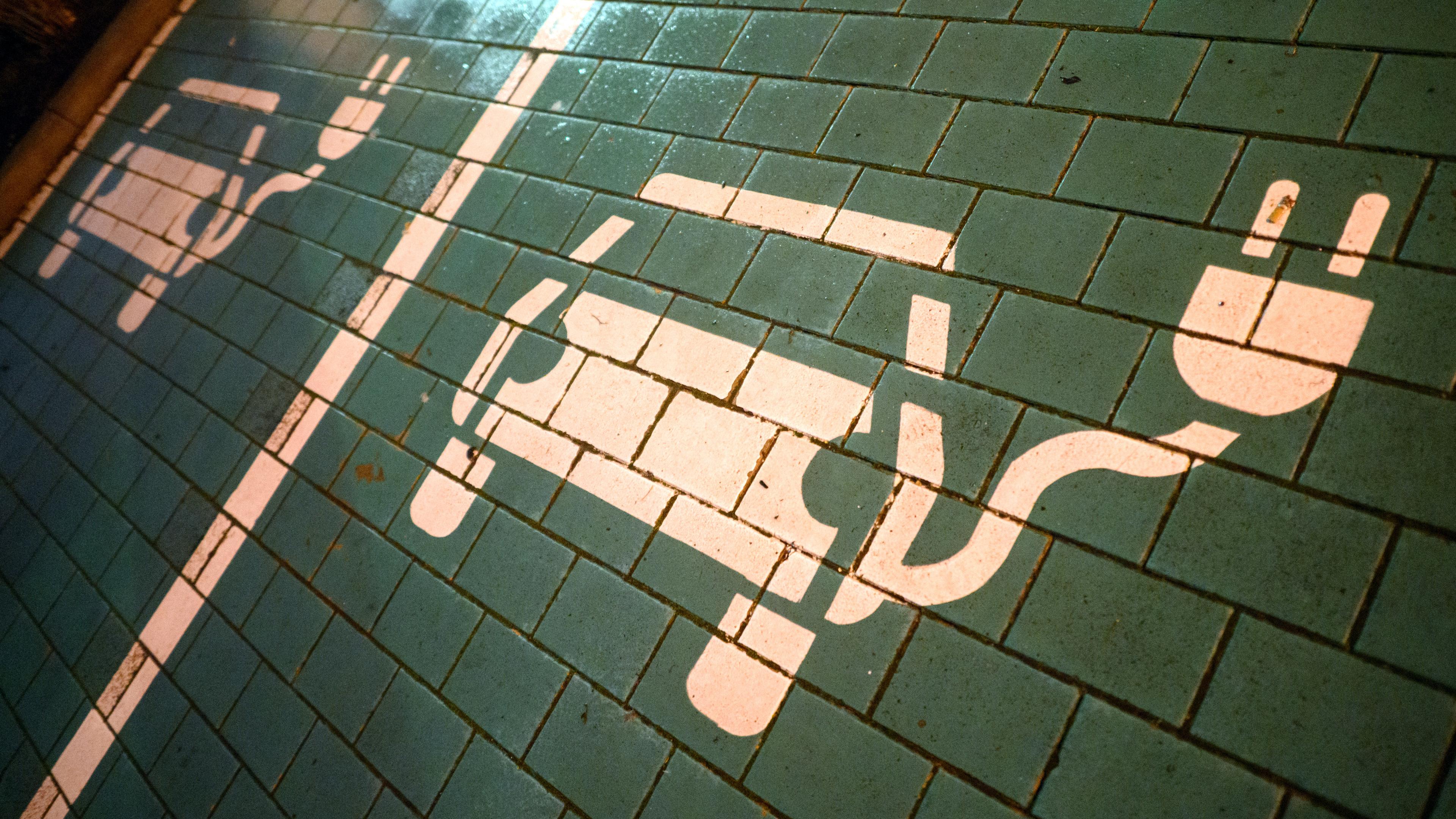 Symbole markieren Parkplätze mit einer öffentlichen Ladesäule für Elektroautos an einem Einkaufszentrum.