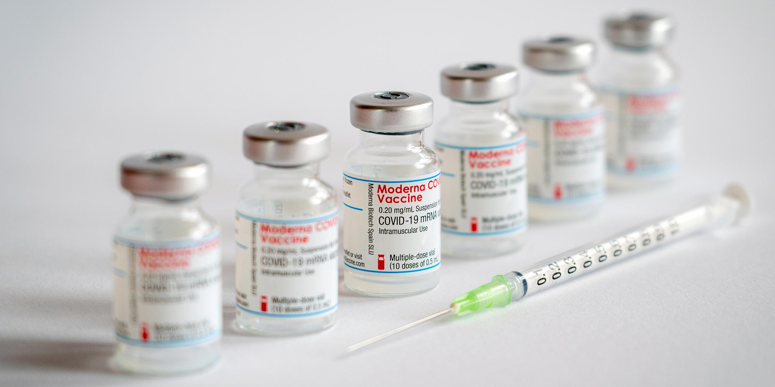 Impfampullen der Firma Moderna stehen hinter einer Impfspritze nebeneinander.