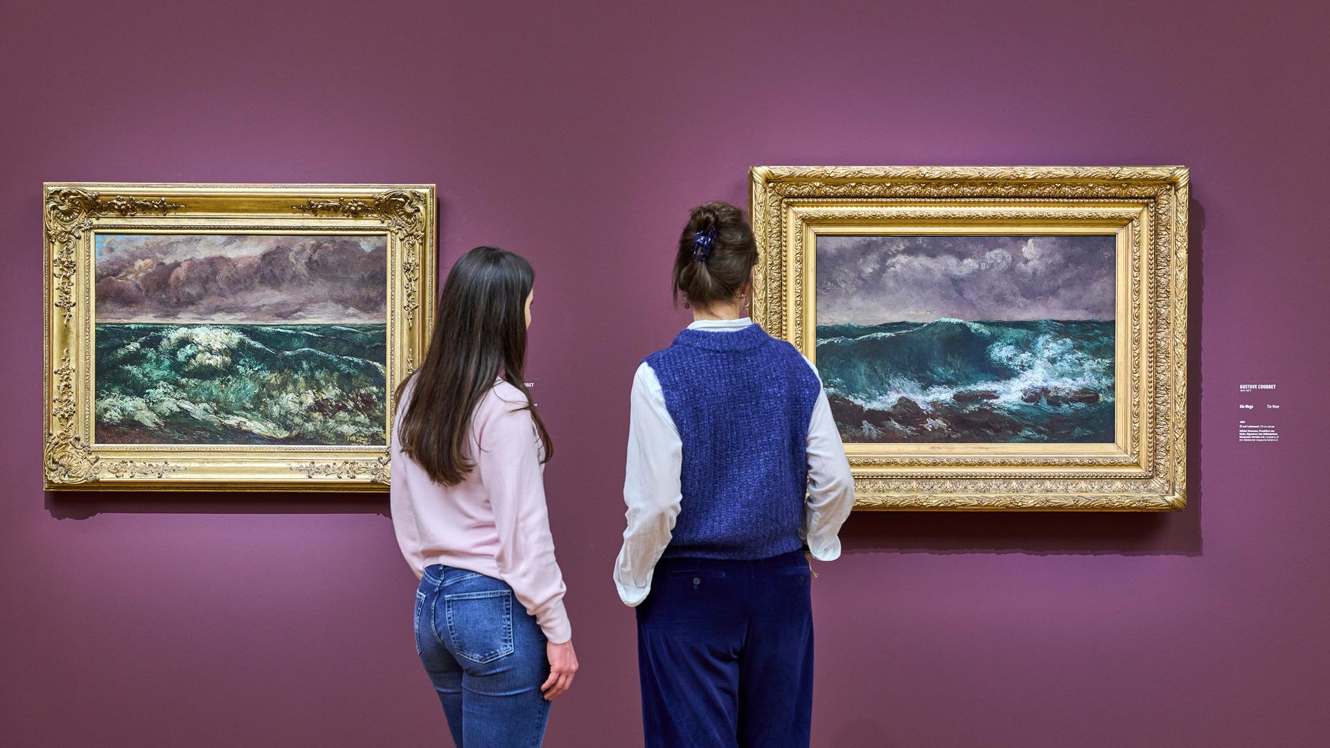 Zwei Personen sehen sich Gemälde von Meereswellen an.