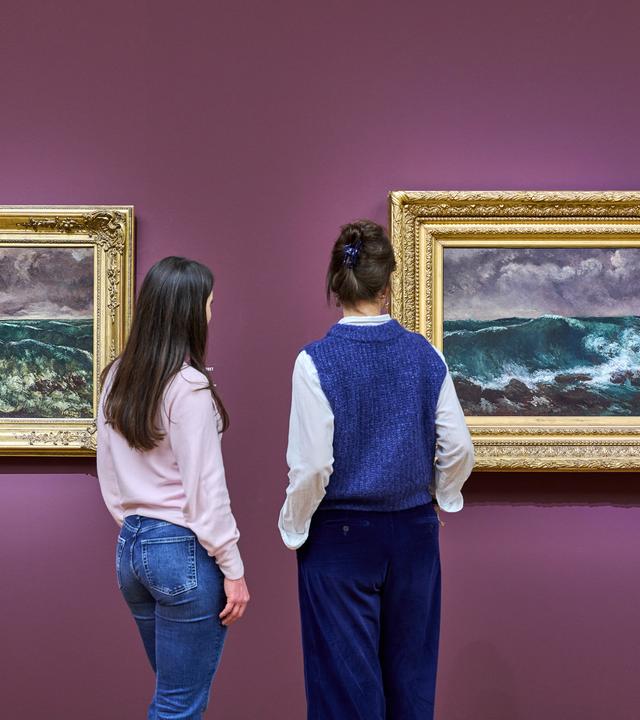 Zwei Personen sehen sich Gemälde von Meereswellen an.